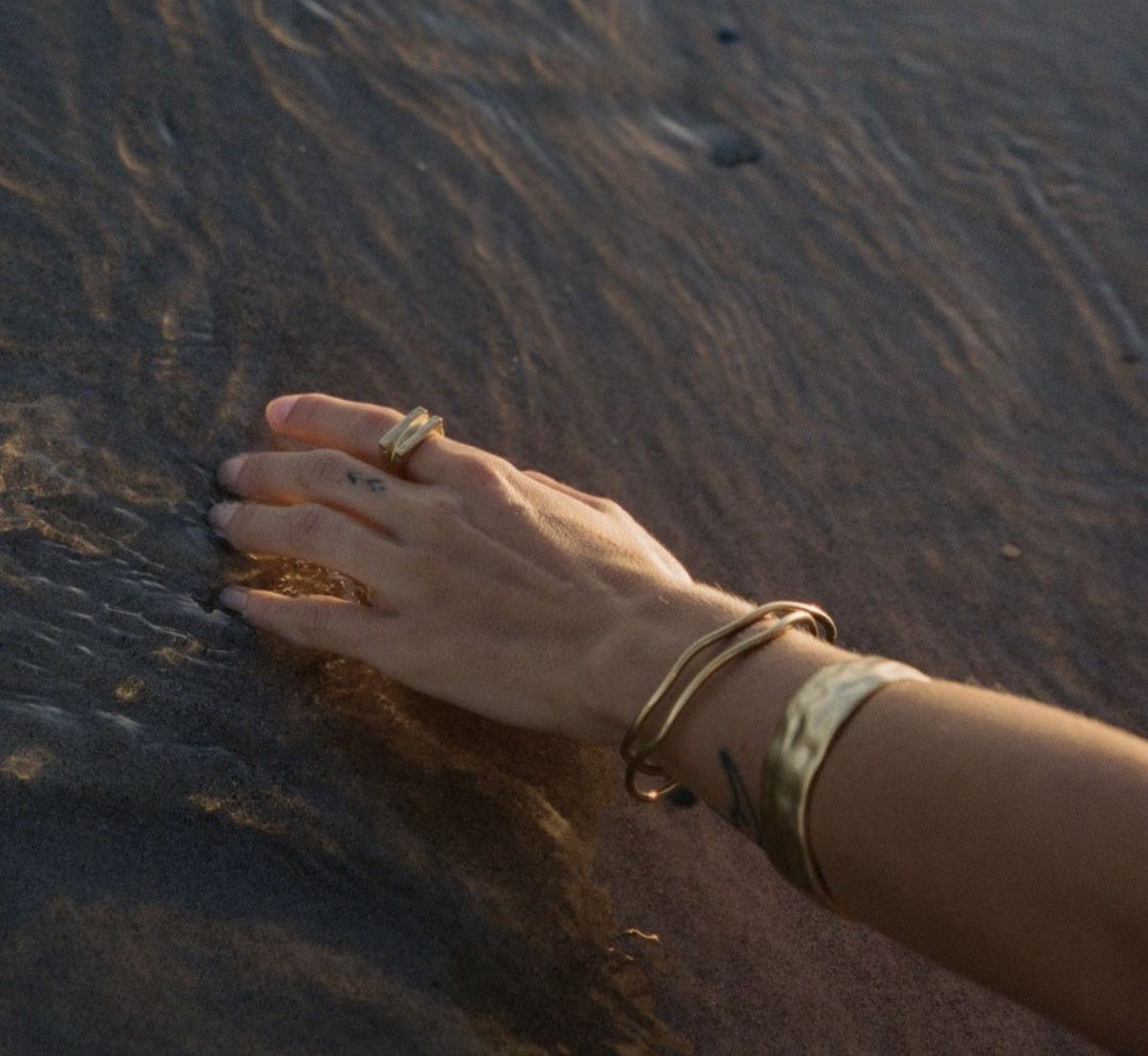Hand with gold ring and bracelets on a textured surface