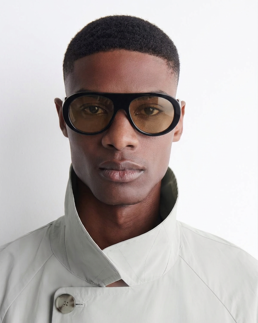 Man wearing a light gray jacket and black sunglasses against a white background