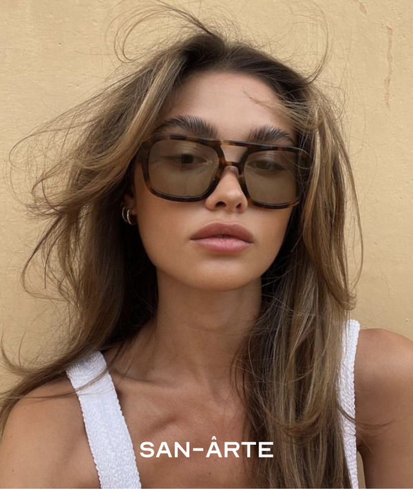 Woman wearing sunglasses with a beige background and 'SANÜaRTE' branding.